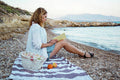 Young Woman Reading A Book On The Pebble Beach By The Sea Print